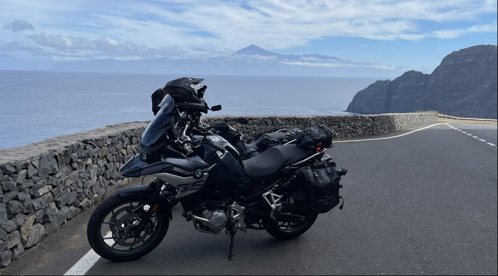 Motorcycle parked on a scenic road with ocean and Tenerife's Mount Teide in the background.